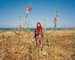 A woman in red scarf standing among flowers.