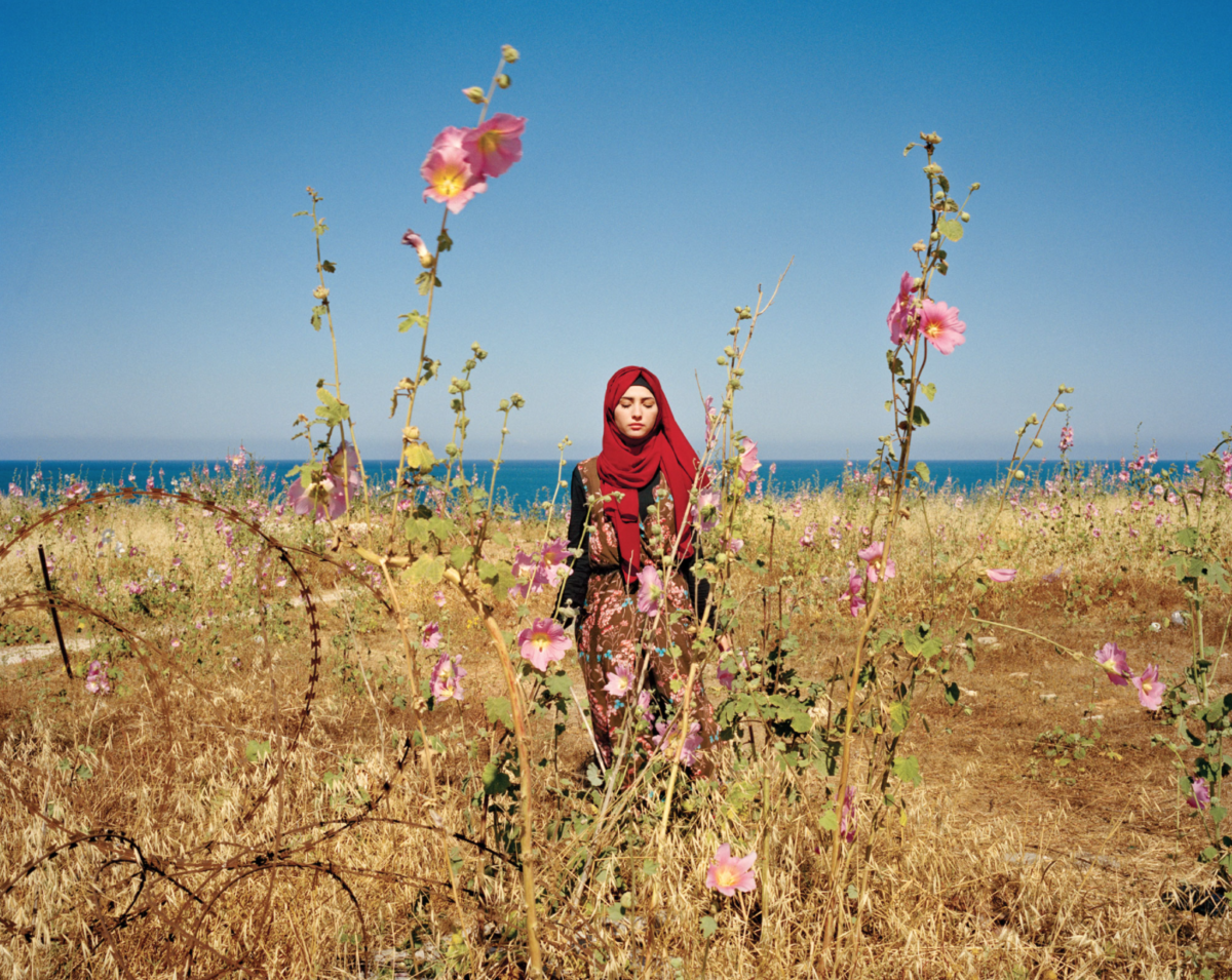 Woman in red hijab among vibrant flowers.