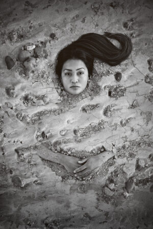 A woman laying in the sand with her hair hanging down.