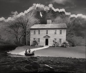 A black and white photo of a house with clouds in the background.