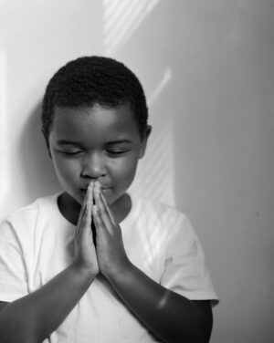 A young boy is praying in front of the wall.