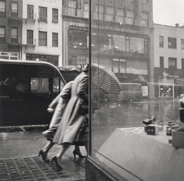 A black and white photo of two people walking down the street