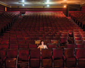 A woman sitting in an empty theater with rows of seats.
