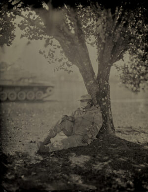 A man sitting under a tree next to a tank.