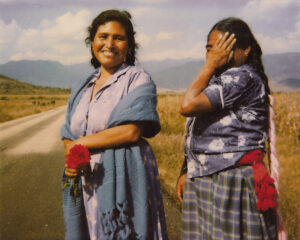 Two women standing on a dirt road near a field.