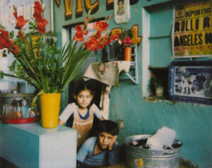 Two children are sitting in a corner of a house.
