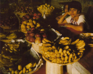 A woman sitting in front of many baskets filled with fruit.