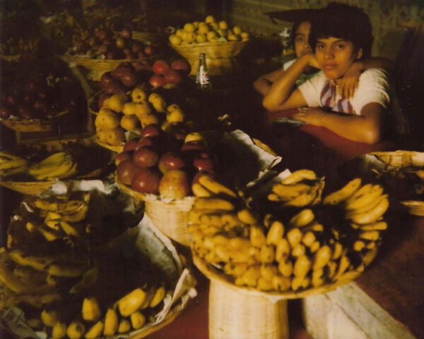A woman sitting in front of many baskets filled with fruit.