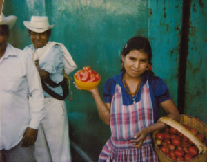A woman holding tomatoes in her hand and wearing an apron.