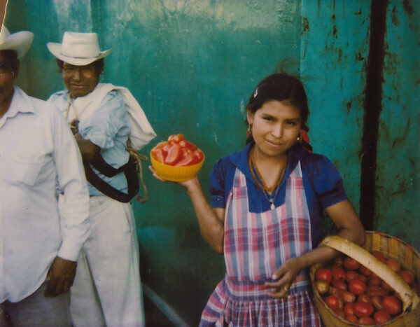 A woman holding tomatoes in her hand and wearing an apron.