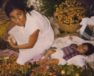 A woman and child sitting on the ground with fruit.