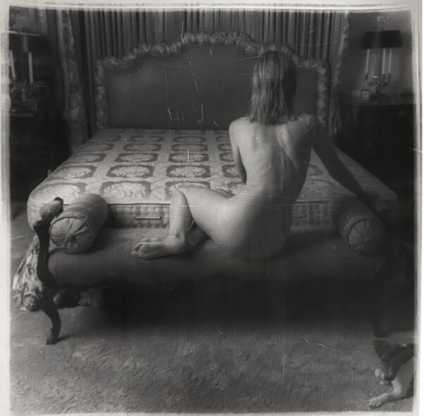 A naked woman sitting on the bed of a bedroom.