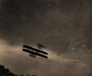A plane flying in the sky with clouds above it.