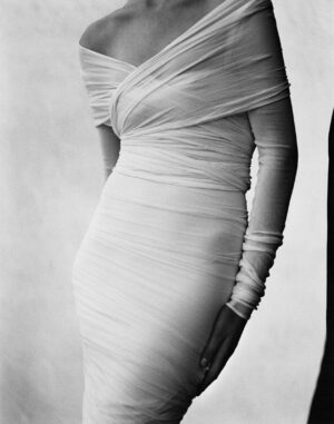 A woman in white dress standing next to wall.
