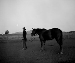 A man standing next to a horse in the middle of an open field.