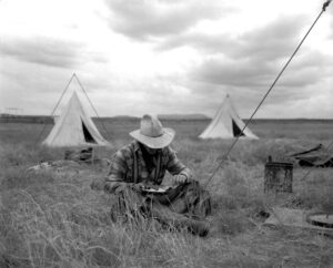 A man sitting in the grass with two tents behind him.