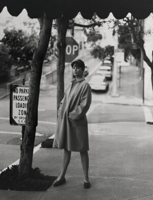 A woman in a trench coat standing on the side of a road.