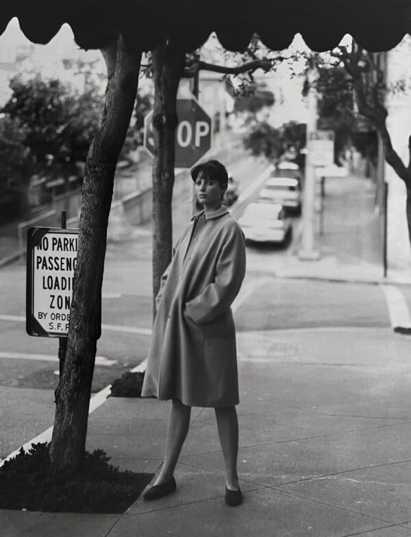 A woman in a trench coat standing on the side of a road.