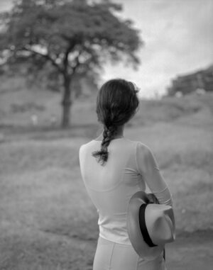 A woman with long hair and a hat is looking out at the trees.