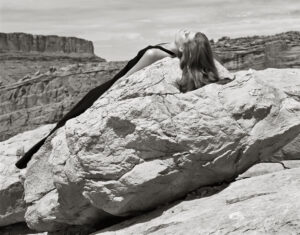 A woman with long hair is sitting on top of a rock.