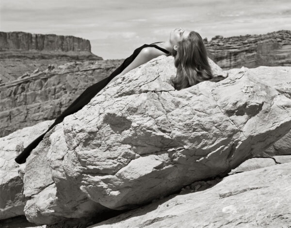 A woman with long hair is sitting on top of a rock.