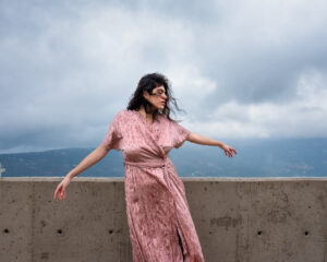 A woman in pink dress standing on top of a concrete wall.