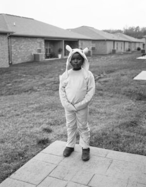 A young boy in bunny costume standing on the sidewalk.