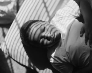 A young child sleeping on the ground in front of a fence.