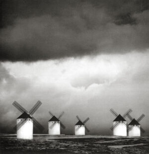 A group of five windmills in the middle of an ocean.