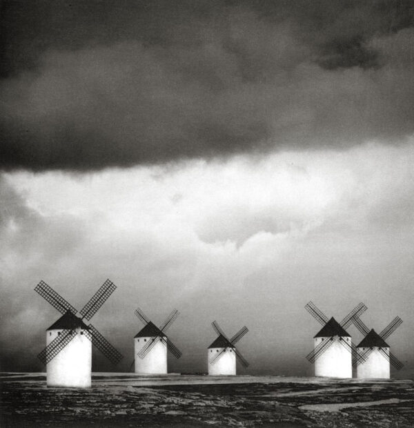 A group of five windmills in the middle of an ocean.