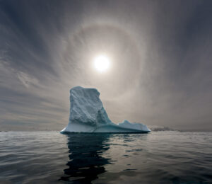 A large iceberg floating in the ocean under an overcast sky.