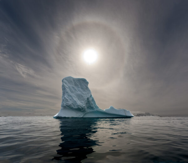 A large iceberg floating in the ocean under an overcast sky.