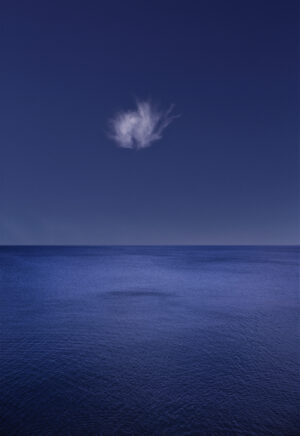 A cloud is seen in the sky over the ocean.