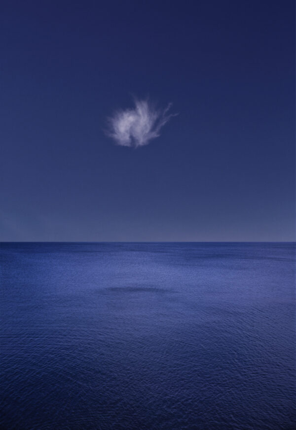A cloud is seen in the sky over the ocean.