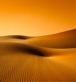 A desert with sand dunes and orange sky.