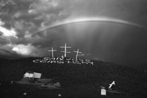 A rainbow over three crosses on top of a hill.