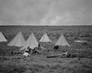 A group of people sitting in the grass near tents.