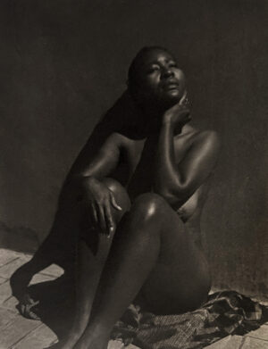 A black woman sitting on the ground with her hand under her chin.