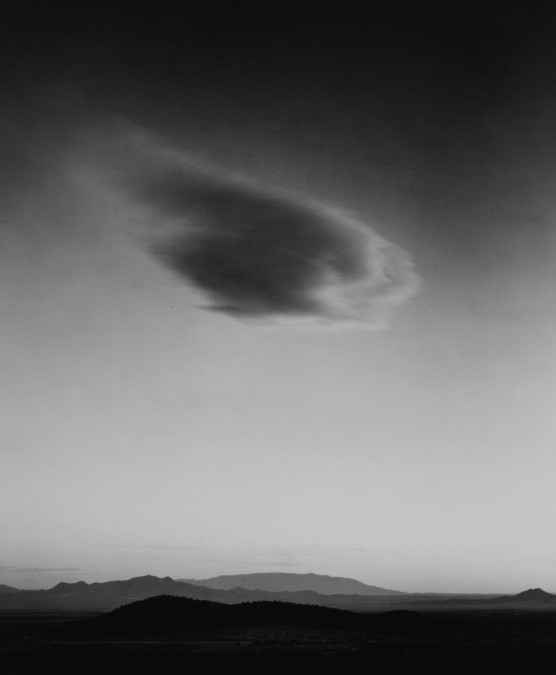 A woman and man sitting on the ground in front of a bench.