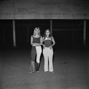 Two women standing in a parking lot at night.