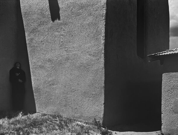 A black and white photo of a person standing in front of a wall.