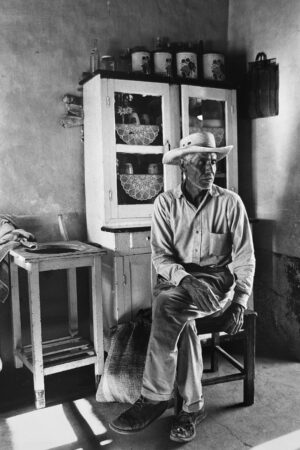 A man sitting on top of a chair in front of a cabinet.