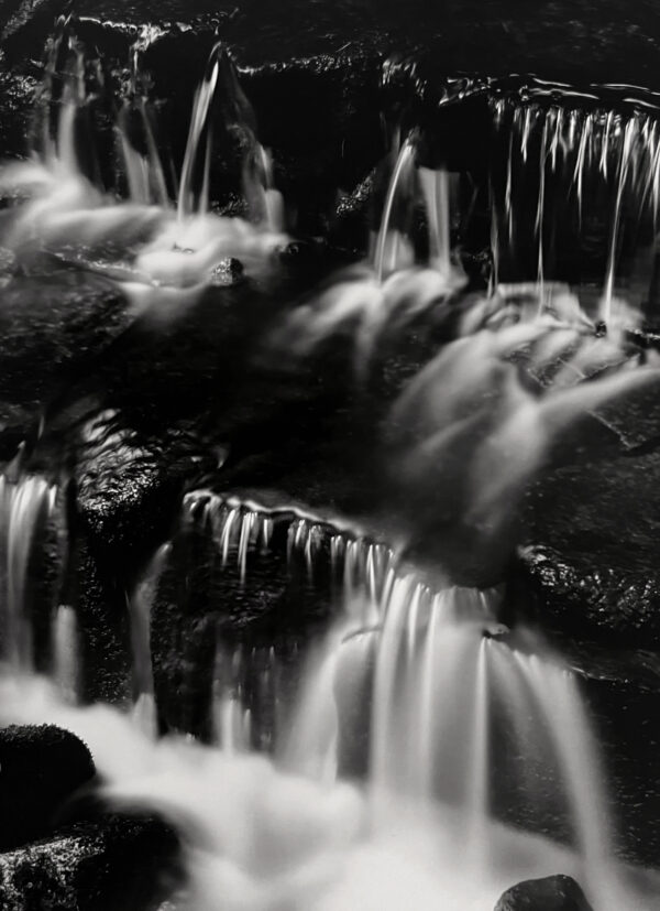 A black and white photo of some water flowing over rocks.