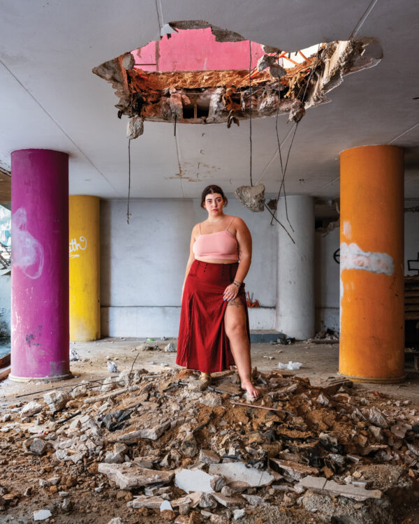 A woman in a pink top and red skirt standing on rubble.