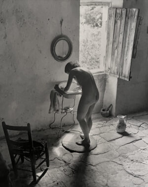 A naked man standing in front of a sink.