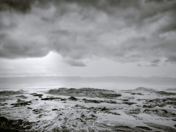 A black and white photo of the ocean with clouds overhead.
