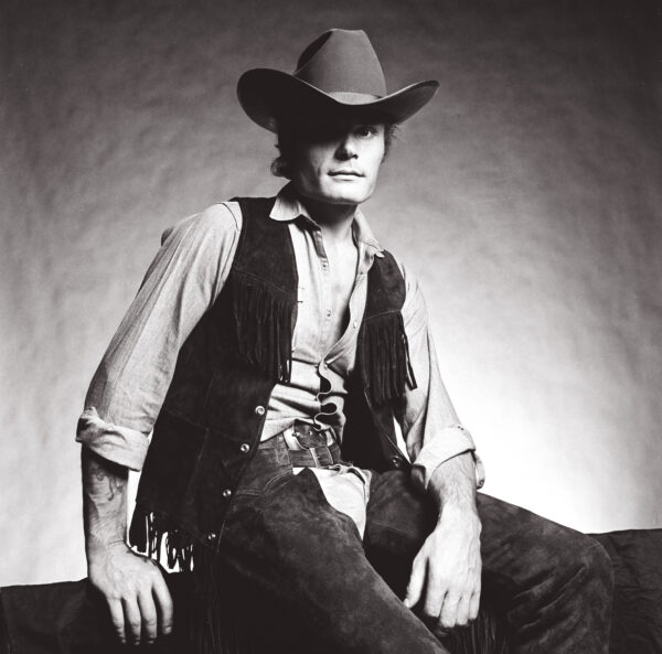 A man in cowboy hat sitting on the ground.