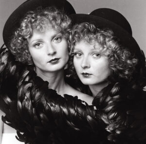 Two women in hats and feathers posing for a picture.