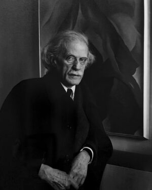 A man in suit and tie sitting next to a painting.