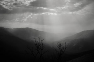 A black and white photo of the sun shining through clouds.